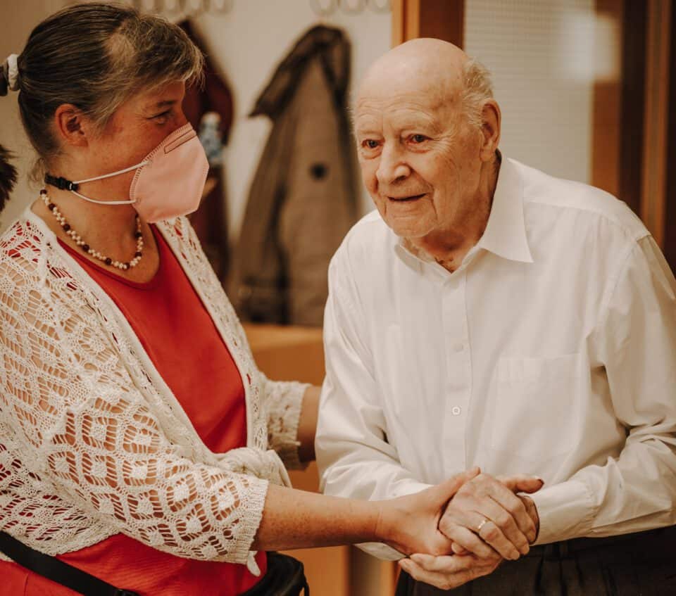 Foto einer Pflegekraft, die sich liebevoll um einen älteren Heimbewohner kümmert